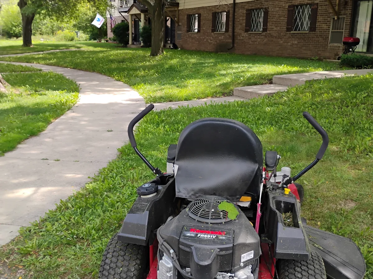 Zero-turn mower cutting grass beside a curved sidewalk